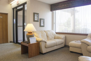 Lobby with cream leather couches, side table with lamp turned on, and large window.